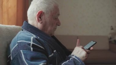 Akıllı telefonlu yaşlı bir adam koltukta oturuyor ve sosyal medyada kayıyor.. 