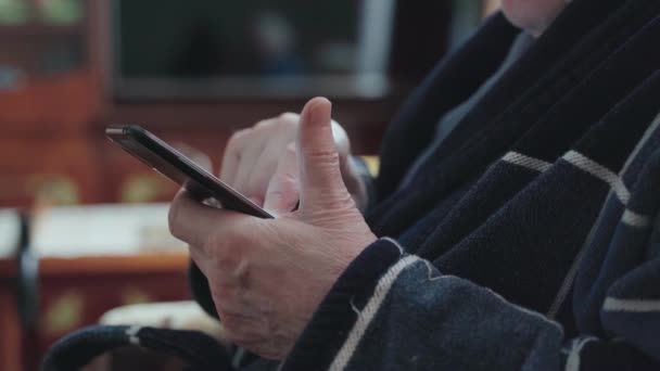 Hombre mayor con teléfono inteligente sentado en un sillón y desplazándose por las redes sociales. — Vídeos de Stock