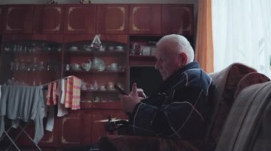 Akıllı telefonlu yaşlı bir adam koltukta oturuyor ve sosyal medyada kayıyor.. 