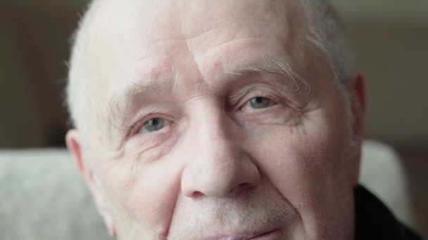 Közelkép egy öreg, mosolygó férfiról, aki a kamerába néz. Nyitott szemű és vidám. Egy boldog idős ember mosolygó kék szemei — Stock videók