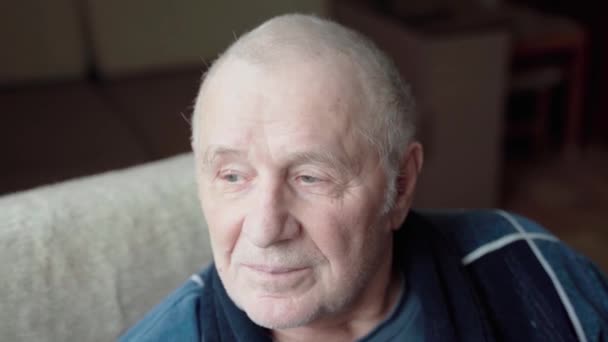 Close-up portret van een oude glimlachende man die naar de camera kijkt. Trieste eenzame man thuis. Eenzaamheid op hoge leeftijd. Handheld video — Stockvideo