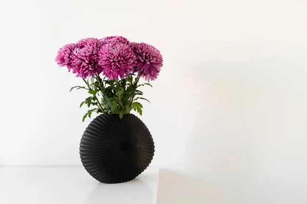 Стильный состав красивых розовых цветков хризантемы, стоящих в черной современной вазе за столом. Концепция культуры Швеции — стоковое фото