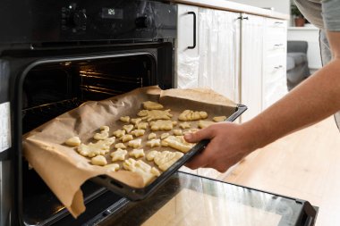Önlüklü bir erkeğin açık fırının önünde durduğu ve tepsiye pasta koyduğu görüntüyü kapat. Stok fotoğrafı
