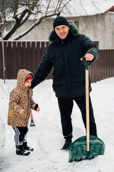 O colapso da neve. Homem sênior com neve de limpeza de crianças em tempo de inverno com uma pá em uma jarda durante o dia frio. Conceito de problemas de inverno — Fotografia de Stock
