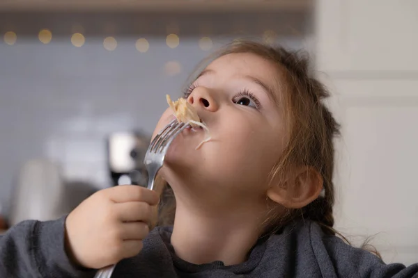 Маленька дівчинка сидить за столом і кладе ложку в рот, при цьому їсть кашу уважно і з апетитом. Стокова фотографія — стокове фото