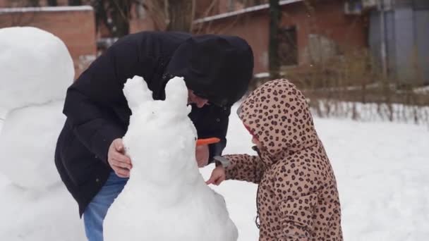 冬の雪の日に遊ぶ父と子供。都会の裏庭で家族と一緒に雪だるまを作る. — ストック動画