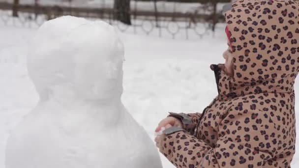 El niño está jugando en el día nevado de invierno. Creación de muñeco de nieve con la familia en el patio trasero urbano. — Vídeo de stock