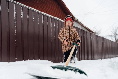 Küçük kızın kardan yolu kürekle temizlemeye yardım ettiği düşük açılı görüntü. Karlı kış bahçesinde oynayan çocuk