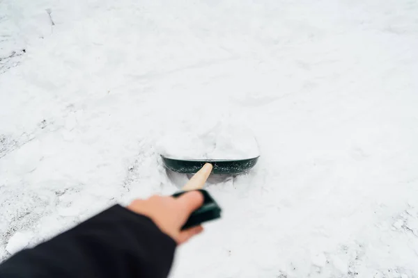 Закрыть большую железную лопату в процессе удаления снега зимой. Неузнаваемый человек держит лопату рукой. — стоковое фото