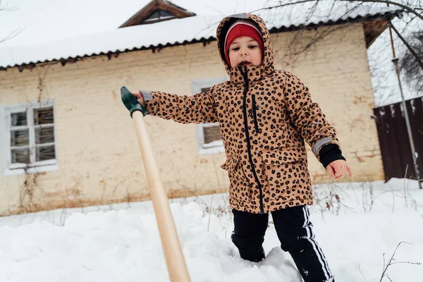 Küçük kızın kardan yolu kürekle temizlemeye yardım ettiği düşük açılı görüntü. Karlı kış bahçesinde oynayan çocuk