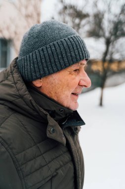 Sıcak giysiler içinde mutlu yaşlı bir adamın yakın plan portresi dışarıda duruyor ve gülüyor.