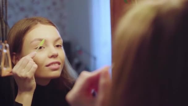 Красива дівчина робить макіяж вдома, виправляючи брови гелем і пензлем — стокове відео