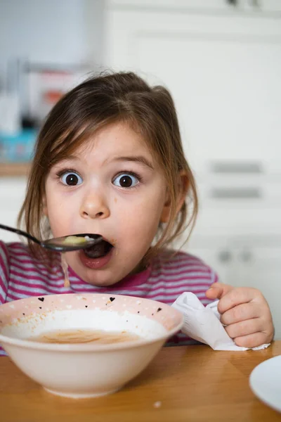 Close up de retrato menina pré-escolar com expressão engraçada comer sopa em casa — Fotografia de Stock