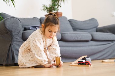 Beyaz elbiseli küçük kız evinde ahşap trenle oynuyor. 
