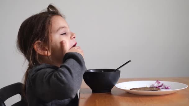 Beautiful child girl eats soup from black bowl with bread and onion. Lifestyle photo of kid in kitchen having a meal. — 图库视频影像