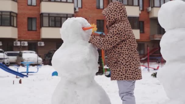 Vater und Kind spielen an einem verschneiten Wintertag. Schneemann mit Familie im städtischen Hinterhof. — Stockvideo