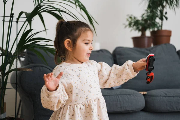 Toddler girl in white dress plays with wooden train at home in the living room