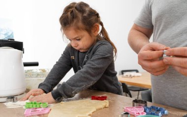 Tanımlanamayan bir adam ve kızının işleme tahtasında bisküvi kesicilerle şeker yaparken görüntülenmiş. Babam yemek tepsisine kurabiye koyuyor.