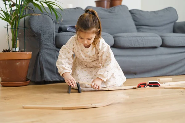 Toddler girl in white dress plays with wooden train at home in the living room