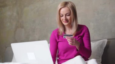 Sarı saçlı beyaz bir kadın internetten kredi kartı ve laptopuyla mal alıyor. Modern alışveriş, fintech konsepti