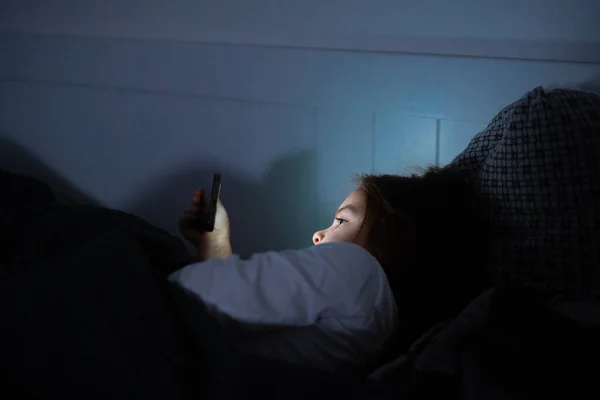 Babymädchen schaut sich Video auf Smartphone im Bett an, bevor sie abends schläft — Stockfoto