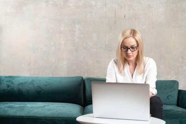 Mulher bonita caucasiana trabalhando remotamente online com laptop no sofá verde. Chamada vídeo freelance de mulher de negócios — Fotografia de Stock