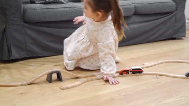 Toddler girl in white dress plays with wooden train at home in the living room. Independent play concept — Stock Video