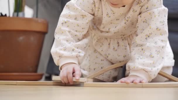Gadis Toddler dalam gaun putih membangun rel kereta api kayu di rumah di ruang tamu — Stok Video