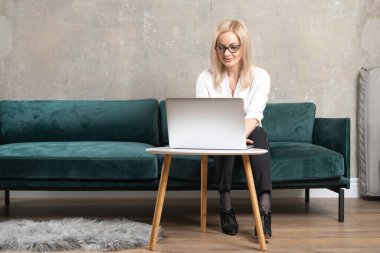 Beyaz tenli güzel bir kadın yeşil kanepede dizüstü bilgisayarla uzaktan çalışıyor. İş kadınının serbest video çağrısı 