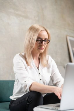 Beyaz tenli güzel bir kadın yeşil kanepede dizüstü bilgisayarla uzaktan çalışıyor. İş kadınının serbest video çağrısı 