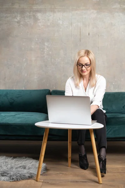 Mulher bonita caucasiana trabalhando remotamente online com laptop no sofá verde. Chamada vídeo freelance de mulher de negócios — Fotografia de Stock