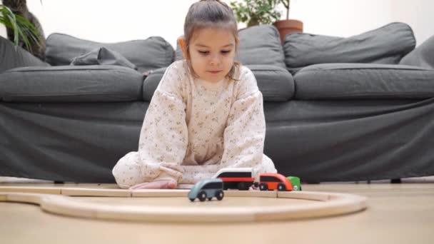 Batole dívka v bílých šatech staví dřevěnou železnici doma v obývacím pokoji — Stock video