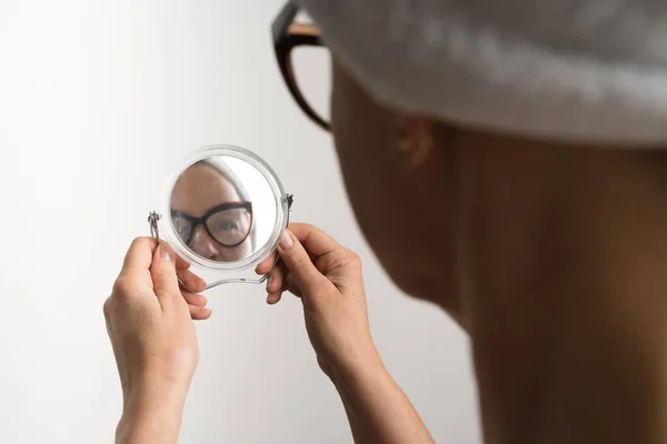 Mujer caucásica de mediana edad después del baño mirando en su reflejo espejo. Rutina diaria de tratamiento facial — Foto de Stock