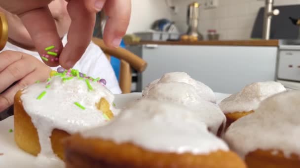 Close-up van de hand kind toe te voegen kleurrijke hagelslag aan cupcake glazuur. Pasen eten in het christendom — Stockvideo