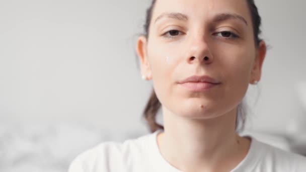 Close-up van vrouwelijke jonge blanke vrouw die serum of olie huidverzorgingsproduct op haar gezicht aanbrengt. Wellness en spa thuis — Stockvideo
