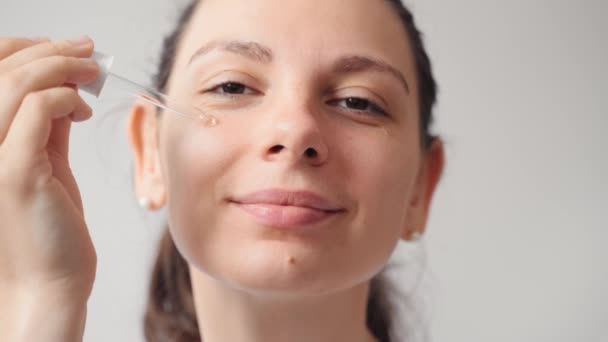Närbild av kvinnliga unga kaukasiska kvinna applicera serum eller släppa olja hudvårdsprodukt på hennes ansikte. Wellness och spa hemma — Stockvideo