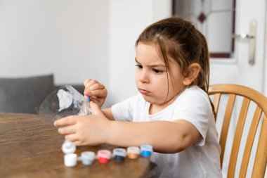 Kafkasyalı anaokulu kızı plastik şişe ve boyalarla el işi yapıyor. Geri dönüşüm atıkları. Sürdürülebilir yaşam tarzı