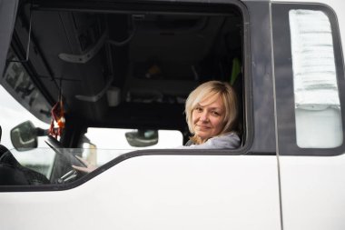 Beyaz, orta yaşlı bir kadın kamyon kullanıyor. Kamyoncu kadın işçi, taşımacılık endüstrisi işgali. 