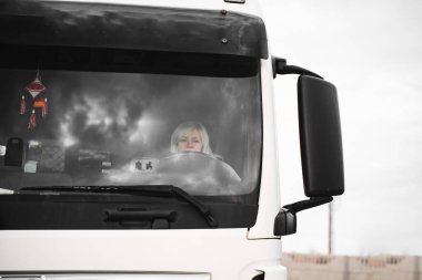 Beyaz, orta yaşlı bir kadın kamyon kullanıyor. Kamyoncu kadın işçi, taşımacılık endüstrisi işgali. 