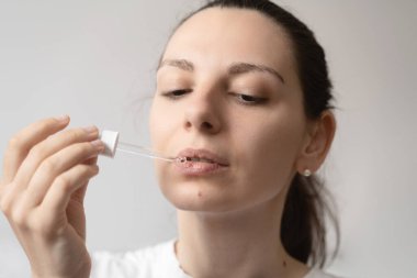 Koyu renk saçlı genç bir kadının cam damlacıkla yağ takviyesi alırken portresi. CBD kenevir yağı dilin üzerine sürülüyor. 