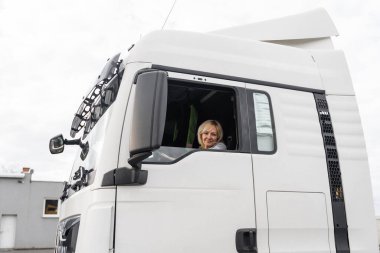 Beyaz, orta yaşlı bir kadın kamyon kullanıyor. Kamyoncu kadın işçi, taşımacılık endüstrisi işgali. 