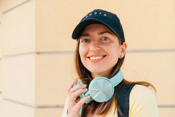 Young woman with mint headphones and black cap outside on the street. — стоковое фото