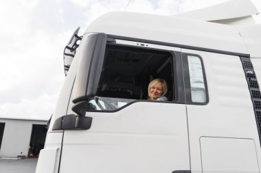 Beyaz, orta yaşlı bir kadın kamyon kullanıyor. Kamyoncu kadın işçi, taşımacılık endüstrisi işgali. 