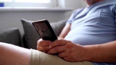 Evde koltukta cep telefonu kullanan olgun bir adam. Son sınıflar için akıllı telefon. Yüksek kalite 4k görüntü