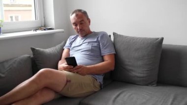 Evde koltukta cep telefonu kullanan olgun bir adam. Son sınıflar için akıllı telefon. Yüksek kalite 4k görüntü