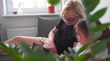 Büyükanne ve anaokulu kızı evde, kanepede birlikte tablet kullanıyorlar. Aile dayanışması. Yüksek kalite 4k görüntü
