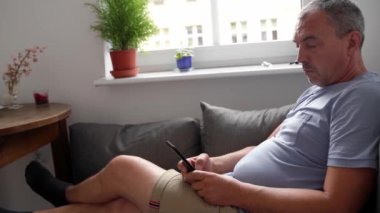 Evde koltukta cep telefonu kullanan olgun bir adam. Son sınıflar için akıllı telefon. Yüksek kalite 4k görüntü