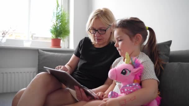 ソファの上の自宅で一緒にタブレットを使用しておばあちゃんと就学前の女の子 家族の団結時間 高品質4K映像 — ストック動画