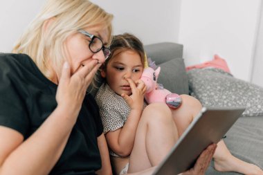 Büyükanne ve anaokulu kızı evde, kanepede birlikte tablet kullanıyorlar. Aile dayanışması. Yüksek kalite fotoğraf