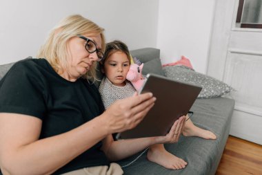 Büyükanne ve anaokulu kızı evde, kanepede birlikte tablet kullanıyorlar. Aile dayanışması. Yüksek kalite fotoğraf